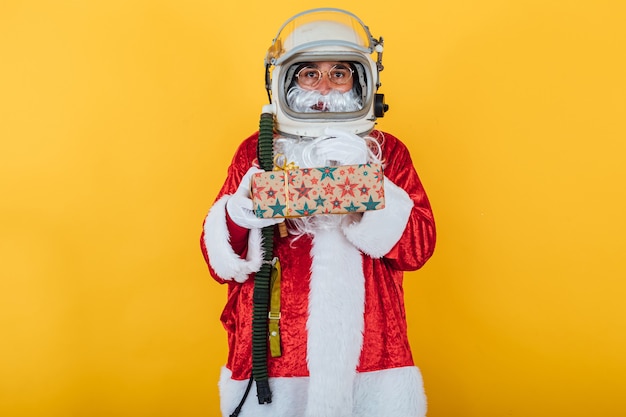 Weihnachtsmann mit Astronautenhelm, der ein Geschenk auf Gelb hält