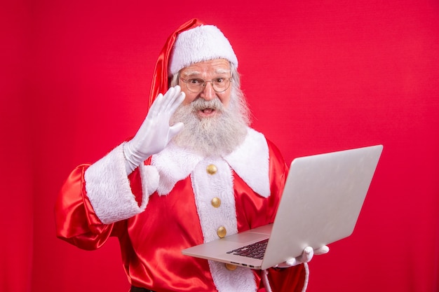 Weihnachtsmann mit einem Laptop auf rotem Grund.
