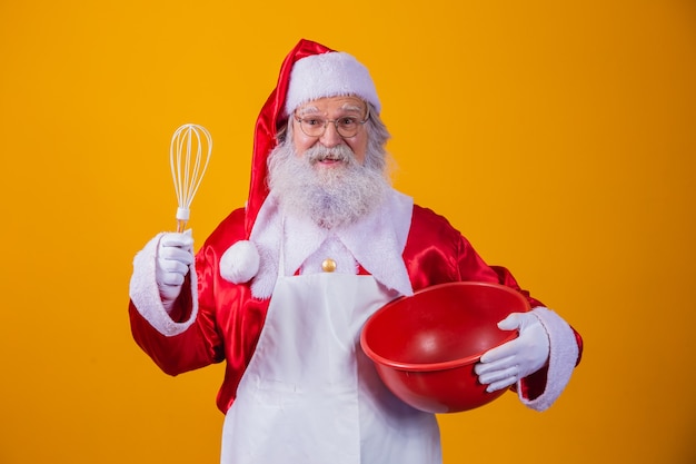 Weihnachtsmann mit einer Schüssel, die Kuchen auf gelbem Hintergrund schlägt