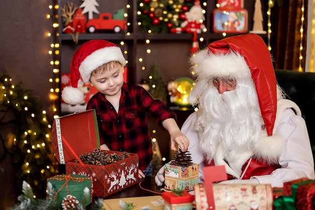 Weihnachtsmann mit kleinem Jungenassistenten, der Weihnachtsgeschenke für Kinderkonzept des neuen Jahres verpackt