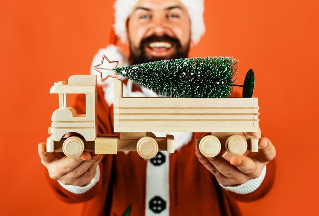 Weihnachtsmann mit kleinem weihnachtsbaum auf hölzernem spielzeug-lkw-lieferservice frohes neues jahr