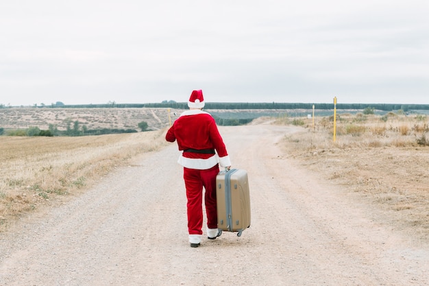 Weihnachtsmann mit Reisekoffer in ländlicher Landschaft