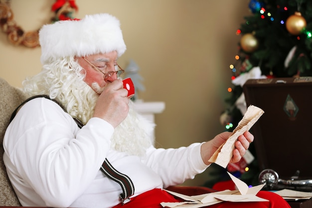 Weihnachtsmann sitzt mit Kinderbriefen im bequemen Stuhl in der Nähe des Kamins zu Hause