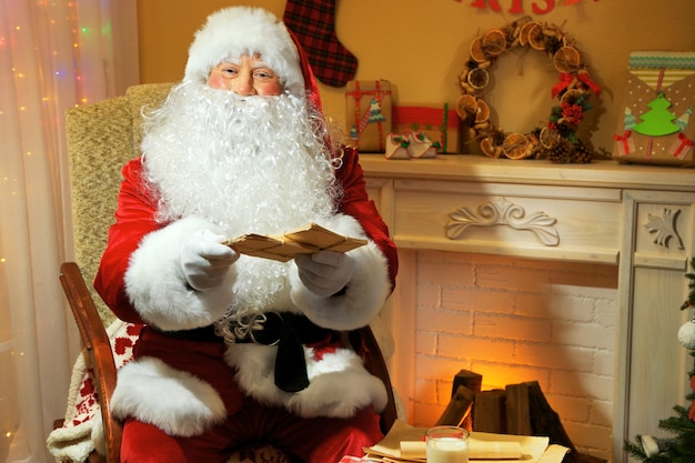 Weihnachtsmann sitzt mit Kinderbriefen im bequemen Stuhl in der Nähe des Kamins zu Hause