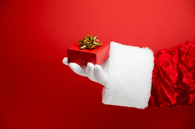 Weihnachtsmannhand mit roter Geschenkbox mit goldener Schleife auf Rot