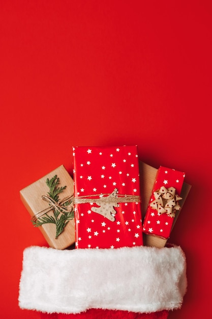 Weihnachtsmannshut mit Geschenkkisten auf rotem Hintergrund Weihnachtgeschenke und Weihnachtenhut auf rotem hintergrund Weihnachtgeschenke