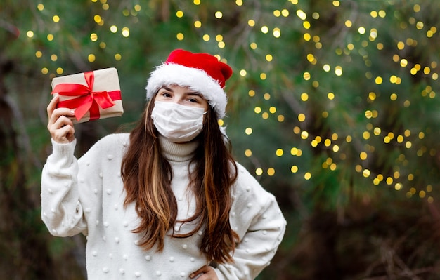 Foto weihnachtsmasken-glückwunschfrau in medizinischer maske, die geschenkbox gibt