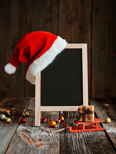 Weihnachtsmodell-Layout für ein frohes neues Jahr. Festliche Komposition mit Weihnachtsdekorationen und Schnee mit leerem Platz für Text. Schwarzer Tafelrahmen mit roter Weihnachtsmütze