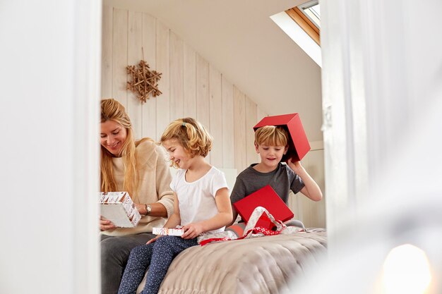 Foto weihnachtsmorgen in einem einfamilienhaus eine mutter und zwei kinder sitzen auf einem bett und öffnen geschenke