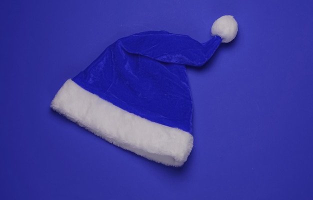 Weihnachtsmütze auf blauem Hintergrund. Neujahr, Weihnachten minimalistisches Konzept. Ansicht von oben, Studioaufnahme.