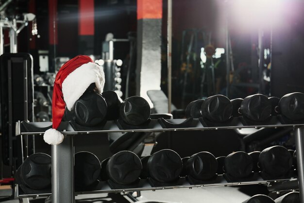 Weihnachtsmütze auf dem Stand mit Hanteln im modernen Fitnessstudio