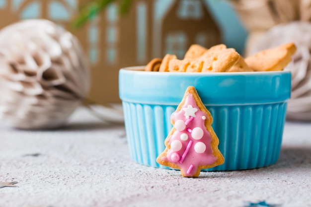 Weihnachtsplätzchen Fichte mit rosa Zuckerguss werden in der Nähe einer Schüssel Kekse auf einem gedeckten Tisch platziert. Festlicher Genuss. Nahansicht