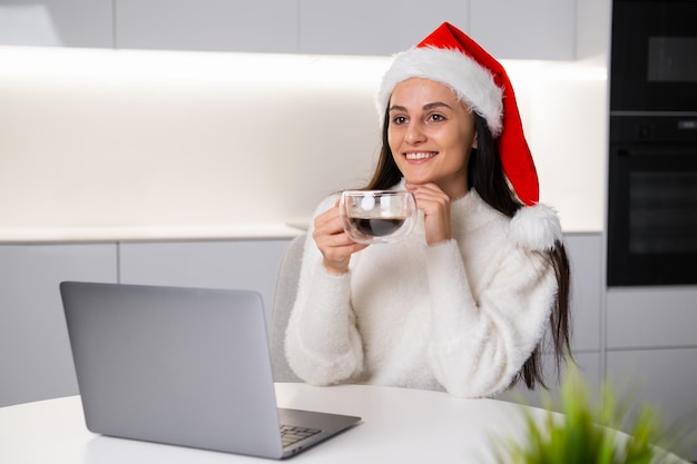 Weihnachtsporträt eines bezaubernden brünetten Mädchens, das eine Tasse Kaffee in der Hand hält, während es am Notizbuch arbeitet