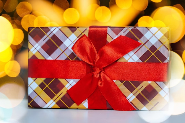 Weihnachtspostkarte mit dekorativer Geschenkbox mit rotem Band auf hellem Bokeh vom Weihnachtsbaum Neujahr