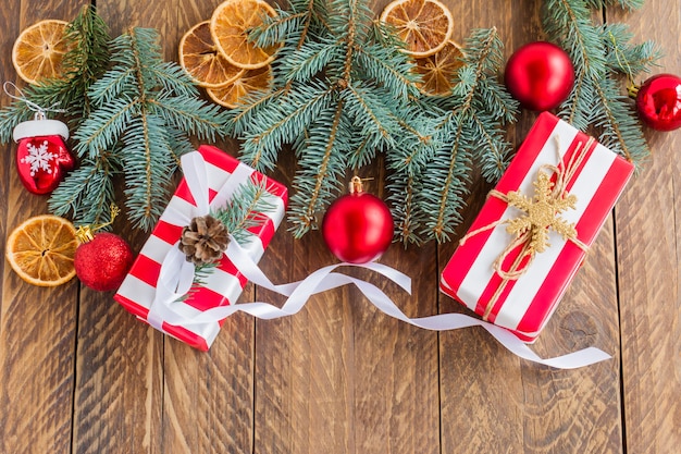 Weihnachtsrahmen aus Tannenzweigen, Kugeln, verpackten Geschenkboxen auf Holzhintergrund. Ansicht von oben