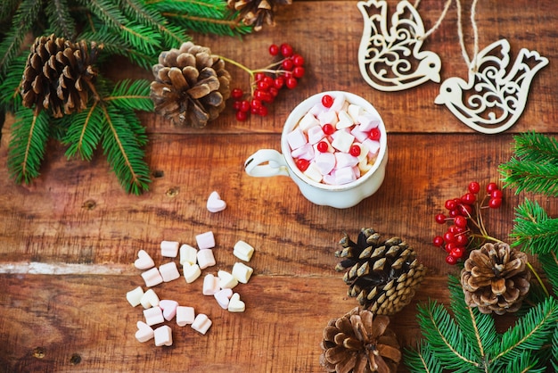 Weihnachtsrahmen. Fichtenzweige, rote Beeren, Vogelfiguren, Geschenk und Tasse mit Marshmallows auf Holzuntergrund