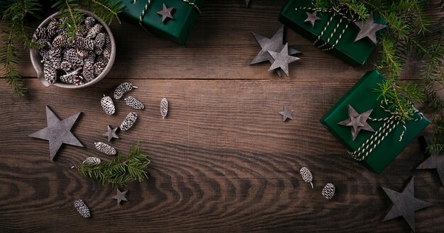 Weihnachtsrahmen mit Geschenkboxen, Holzsterndekorationen, Tannenzapfen und Fichtenzweigen auf dunklem Holzhintergrund. Feiertagshintergrund in den natürlichen Erdfarben.