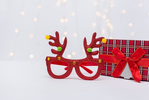 Weihnachtsrote brille mit hirschgeweih und eine geschenkbox auf weißem hintergrund mit bokeh