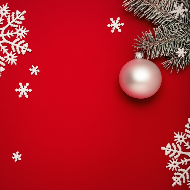 Foto weihnachtsroter hintergrund mit tanne, weißem ball und schneeflocken.