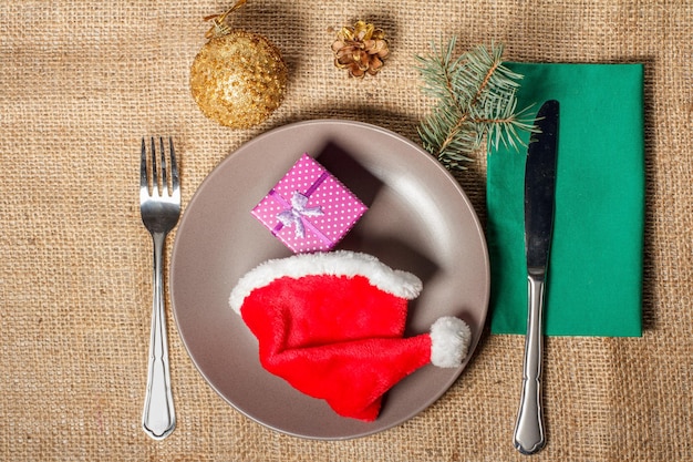 Weihnachtsroter Hut und Geschenk in Geschenkbox auf Tellergabel und Messer auf Serviette