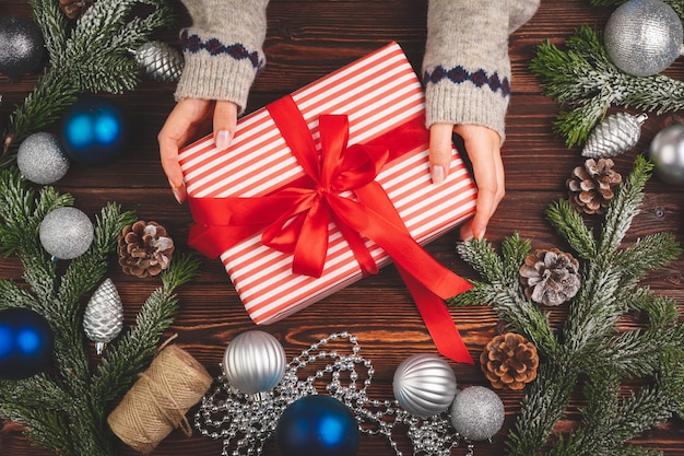 Weihnachtsschmuck auf Holztisch mit dekoriertem Geschenk in den Händen der Frau