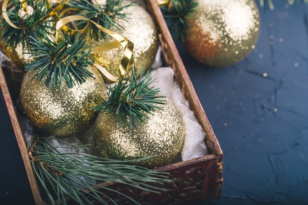 Weihnachtsschmuck, goldene Kugeln, in einer Holzkiste mit Tannenzweigen auf dunkelgrauem Hintergrund, Weihnachtskarte