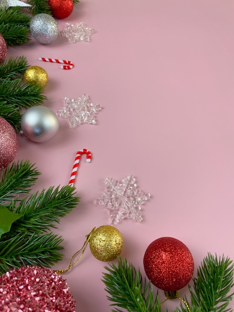 Weihnachtsschmuck, Kiefernblätter, goldene Kugeln, Schneeflocken, rote Kugeln auf rosa Hintergrund