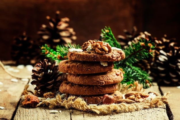 Weihnachtsschokoladenkekse mit Nüssen, Tannenzweigen, Tannenzapfen und Schneeflocken, selektiver Fokus auf Vintage-Holzhintergrund