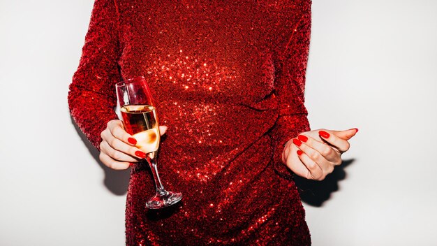 Weihnachtsspaß Glamouröse Frau Partygetränk Festliche Feier Nicht erkennbare Dame in rotem Spangle-Kleid mit einem Glas Champagner, das mit den Fingern isoliert weiß klatscht