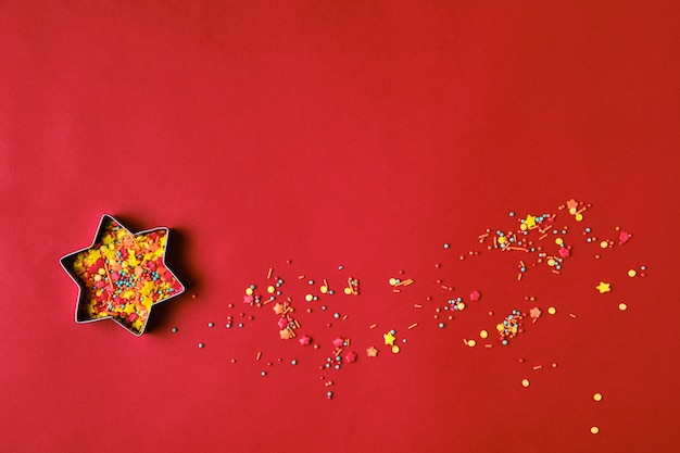 Weihnachtssternform-Lebkuchen-Ausstecher gefüllt mit bunten Zuckerstreuseln auf rotem Hintergrund. Platz kopieren. Weihnachtskarte