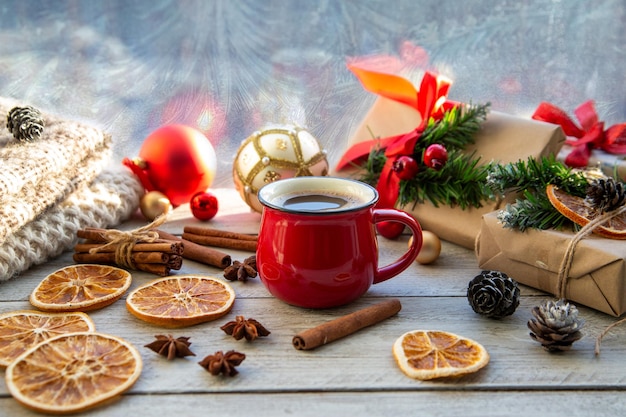 Weihnachtsstimmung Urlaubsatmosphäre Rote Tasse Kaffee Weihnachtsgeschenkboxen Weihnachtsbaum goldene Kugel Kegel Sternanis Zimt auf einer hölzernen Fensterbank