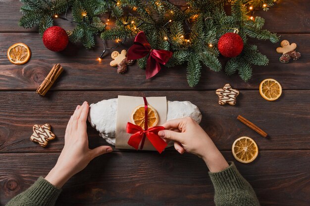 Foto weihnachtsstollen mit marzipan und getrockneten früchten auf dunklem hintergrund feierliche weihnachtsliche licht-ferien-stimmung fröhliche zeit weibliche hände dekorieren stollen für den markt