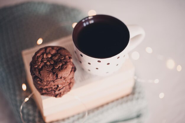 Weihnachtstasse frischer schwarzer Tee mit amerikanischen Schokoladenplätzchen über Licht an der Hintergrundnahaufnahme. Guten Morgen. Frühstück. Winterferienzeit. Leckerer Imbiss.