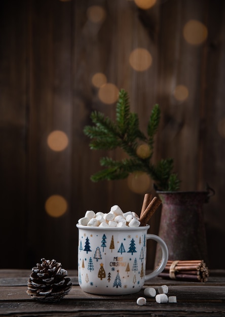 Weihnachtstasse Kakao und Marshmallow mit Zimt auf einem alten braunen Holztisch mit Bokeh, Zapfen und Tanne. Neujahrsstimmung. Vorderansicht und Kopierbereich