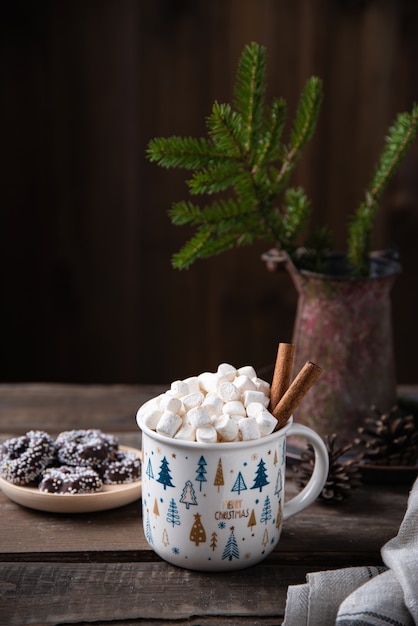 Weihnachtstasse Kakao und Marshmallow mit Zimt auf einem alten braunen Holztisch mit Keksen und Tanne. Neujahrsstimmung. Vorderansicht und Kopierbereich