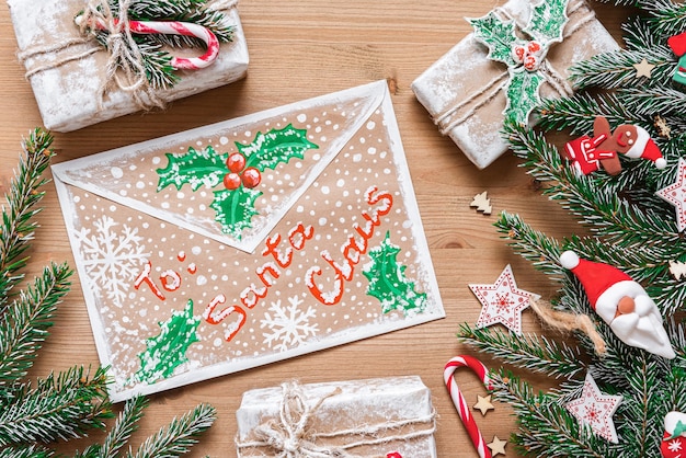 Weihnachtsumschlag auf einem hölzernen Hintergrund mit Tannenzweigen und verschiedenen Geschenken.
