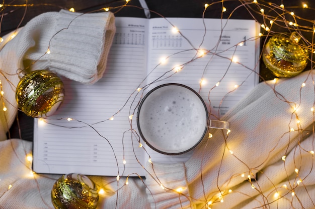 Foto weihnachtswohnung komposition mit warmem pullover, weihnachtsbeleuchtung, notizblock und kaffee.