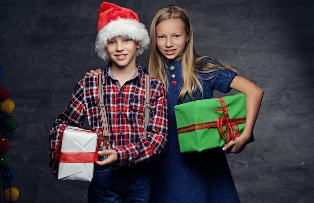 Weihnachtszeit. Teenager in Santa's Hut und blondes Mädchen hält Geschenkboxen auf grauem Hintergrund.