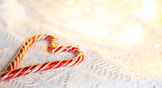 Weihnachtszuckerstange gestreifter Weihnachtsmann in Form von Herzen auf einer weißen Strickdecke. Ein Symbol der Liebe, ein Geschenk an einen geliebten Menschen, ein süßer Leckerbissen. Neujahr. Platz für Text