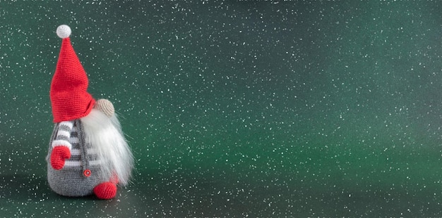 Weihnachtszwerg im Feiertagsbanner des roten Hutes auf dunkelgrünem Winterhintergrund