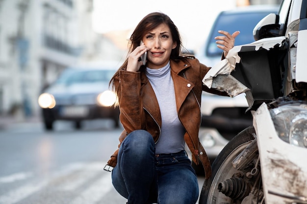 Weinende Frau, die nach einem Autounfall mit dem Handy telefoniert und Pannenhilfe fordert