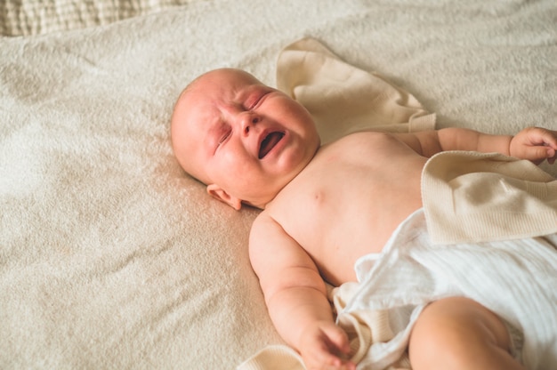 Weinendes Baby, das auf dem Bett liegt