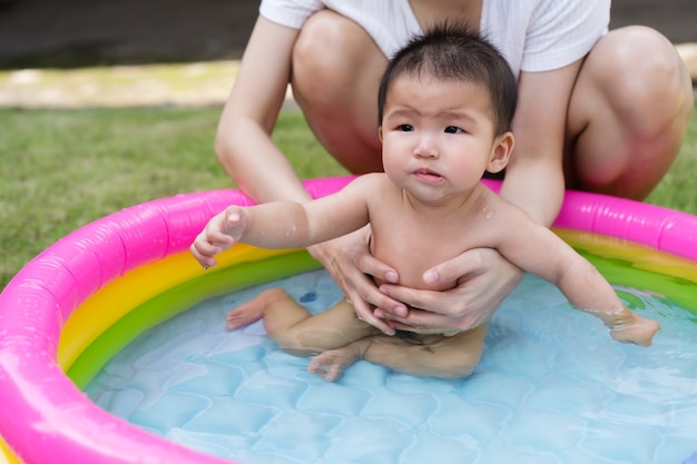 Weinendes Baby, das von Mutter getragen wird, genießt im aufblasbaren Pool