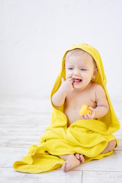 Weinendes kleines Mädchen unter einem gelben Handtuch im Badezimmer nach dem Baden oder Waschen des Babyhygienekonzepts