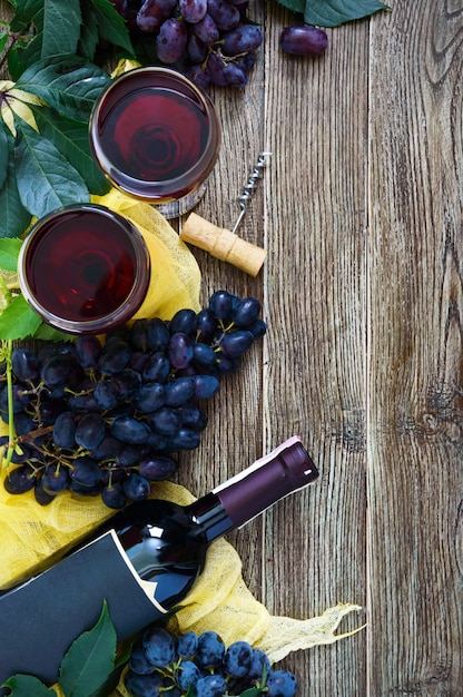 Weingläser mit Rotwein, Flasche, Korkenzieher, blaue Trauben, Blätter auf einem Holztisch. Weinhintergrund mit Kopienraum. Ansicht von oben, flach