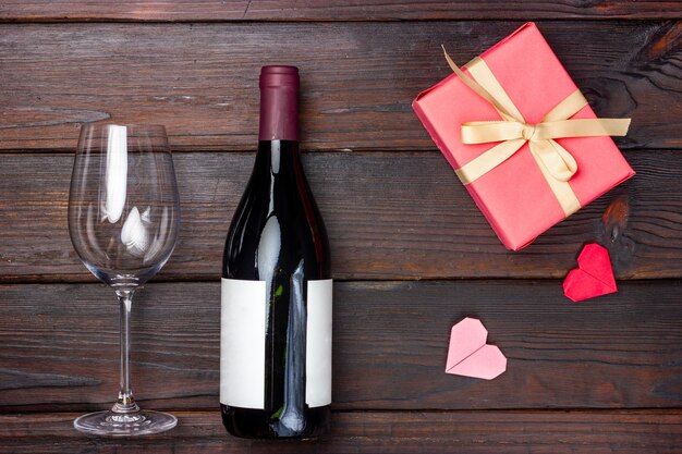 Weinglas, Flasche Rotwein und rosa Geschenk auf einem dunklen Hintergrund.
