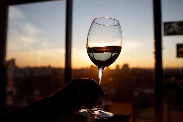 Weinglas über Sonnenuntergang. Fenster und Stadt im Hintergrund.