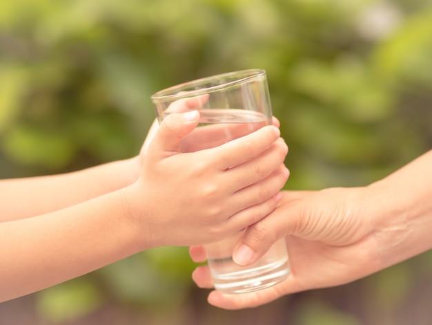 Weinlesefrauenhand der Nahaufnahme, die dem Kind Glas Süßwasser im Park gibt