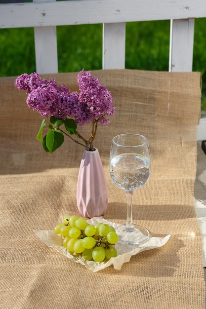 Weintraube Glas Wasser und Vase mit Flieder stehen auf Sackleinen auf Holzboden