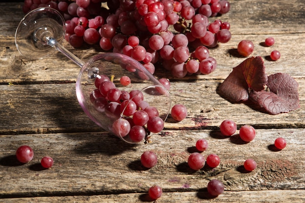 Weintrauben auf einem Holztisch, Weinglas wird umgeworfen, Traubenbeeren werden über die Oberfläche verstreut